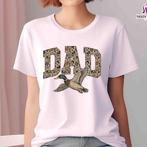 May include: White t-shirt with the word "DAD" in camouflage print with a duck flying above the word.