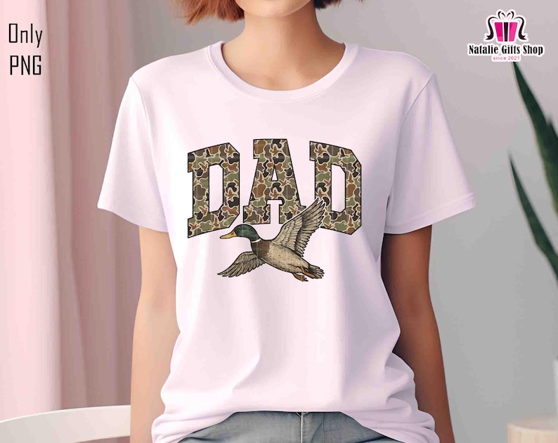 May include: White t-shirt with the word "DAD" in camouflage print with a duck flying above the word.