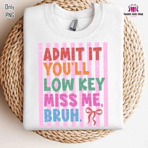 May include: White sweatshirt with the text "ADMIT IT YOU'LL LOW KEY MISS ME, BRUH." in colorful letters. The text is set against a pink striped background. A red bow is at the bottom right. The sweatshirt is on a woven surface.