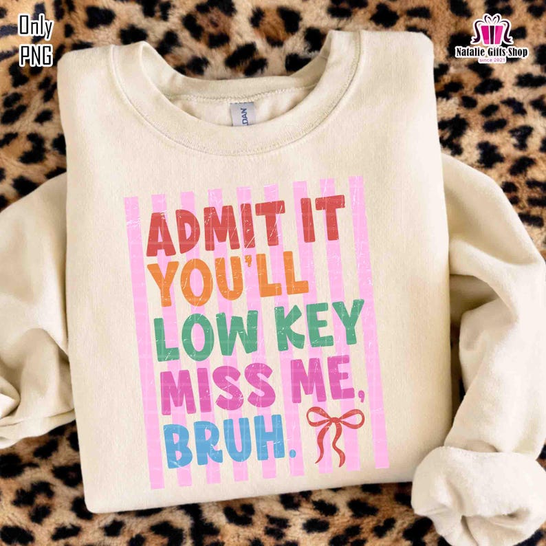 May include: Cream-colored sweatshirt with the text "ADMIT IT YOU'LL LOW KEY MISS ME, BRUH." in a colorful, vertical design. The text is in red, orange, green, pink, and blue. A pink bow is at the bottom. The sweatshirt is on a leopard print background.
