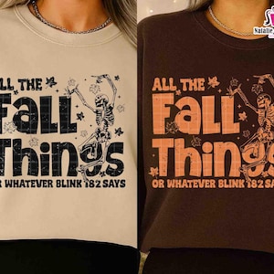 May include: Two sweatshirts, one beige and one brown, each with the text "ALL THE FALL THINGS" and a skeleton graphic. The text "OR WHATEVER BLINK 182 SAYS" is below the main text. The beige sweatshirt has black text and the brown one has orange text.