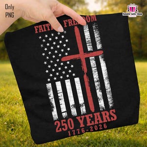 Op de afbeelding: Zwarte stof met een verweerd Amerikaans vlagontwerp, met een rood kruis eroverheen. De woorden "FAITH FREEDOM" en "250 YEARS 1776-2026" zijn in het rood gedrukt. De stof wordt tegen een achtergrond van groen gras gehouden.