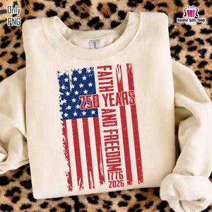 May include: Cream-colored sweatshirt featuring a distressed American flag design. The flag incorporates blue stars and red stripes, with the words "Faith and Freedom" and "250 Years 1776-2026" printed in red. The sweatshirt has a crew neck and long sleeves.