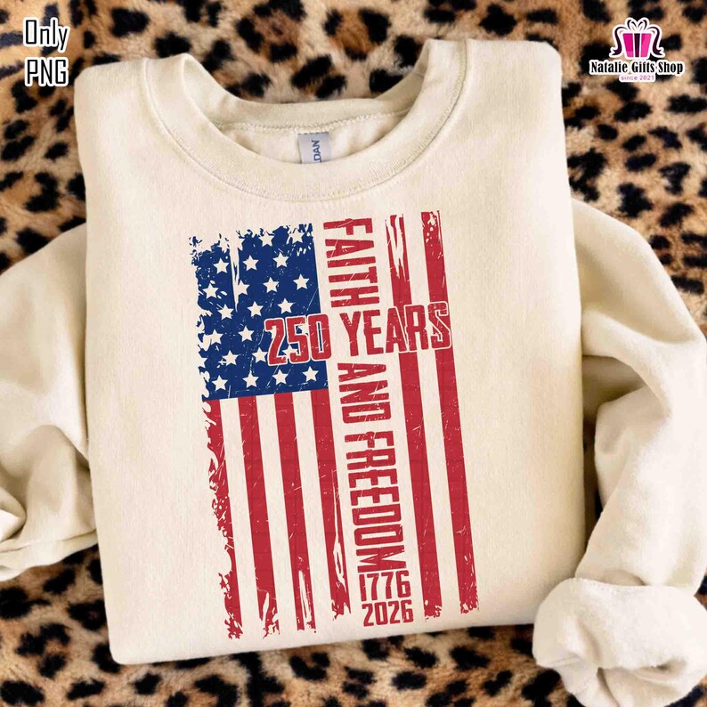 May include: Cream-colored sweatshirt featuring a distressed American flag design. The flag incorporates blue stars and red stripes, with the words "Faith and Freedom" and "250 Years 1776-2026" printed in red. The sweatshirt has a crew neck and long sleeves.