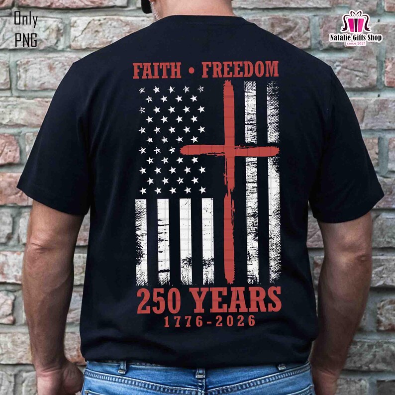 Op de afbeelding: Zwart T-shirt met een verweerd Amerikaans vlagontwerp en een rood kruis. Het shirt toont de woorden "FAITH &bull; FREEDOM" en "250 YEARS 1776-2026", ter herdenking van een belangrijke historische periode.