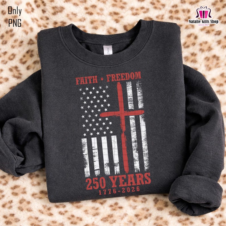 Op de afbeelding: Donkergrijze sweatshirt met een verweerd Amerikaans vlagontwerp en een rood kruis. De tekst "FAITH &bull; FREEDOM" en "250 YEARS 1776-2026" is in het rood gedrukt. De sweatshirt heeft een ronde hals en lange mouwen.