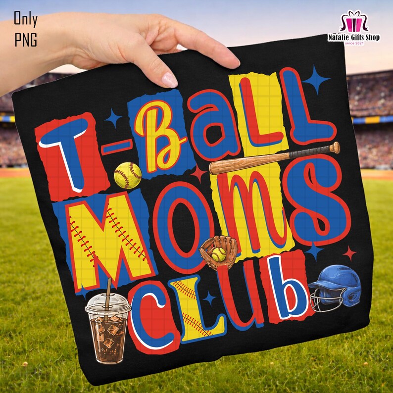 May include: Black t-shirt with a colorful graphic that reads "T-Ball Moms Club." The design includes baseballs, a bat, a glove, and a baseball helmet. A cold drink with ice is also featured in the design.