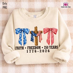 May include: Cream-colored sweatshirt with patriotic graphics. Features a blue bow with white stars, a wooden cross draped with a red, white, and blue scarf, and a red bow. Text reads "FAITH &bull; FREEDOM &bull; 250 YEARS 1776-2026".
