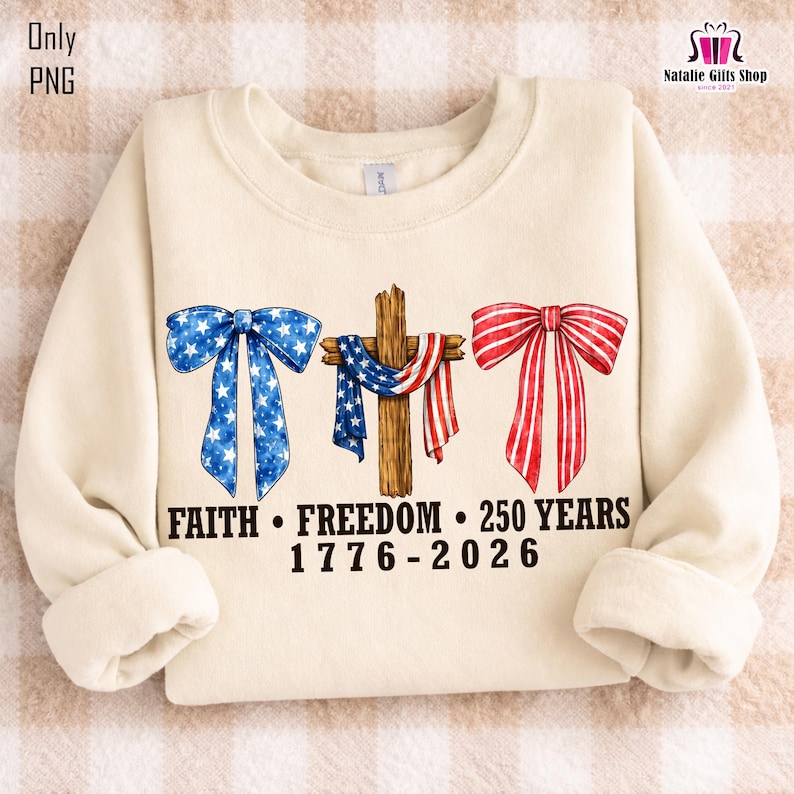 May include: Cream-colored sweatshirt with patriotic graphics. Features a blue bow with white stars, a wooden cross draped with a red, white, and blue scarf, and a red bow. Text reads "FAITH &bull; FREEDOM &bull; 250 YEARS 1776-2026".