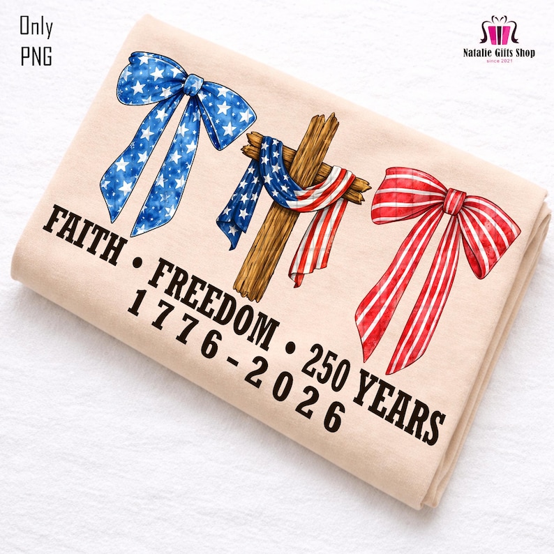 May include: A beige folded t-shirt featuring patriotic designs. It includes a blue bow with white stars, a wooden cross draped with a US flag, and a red and white striped bow. The text reads "FAITH &bull; FREEDOM &bull; 250 YEARS 1776-2026".