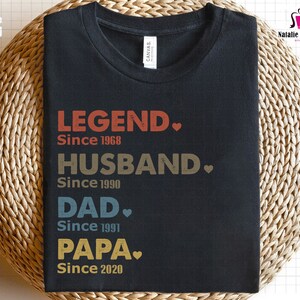 Puede incluir: Camiseta negra con un dise&ntilde;o de estilo vintage que dice "LEGEND. Since 1968", "HUSBAND. Since 1990", "DAD. Since 1991", y "PAPA. Since 2020".