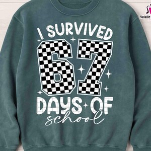 May include: A teal sweatshirt with the text "I SURVIVED 67 DAYS OF school" in white. The numbers "67" are filled with a black and white checkered pattern. The sweatshirt also has the text "PNG, EPS, DXF, SVG" on the left side.