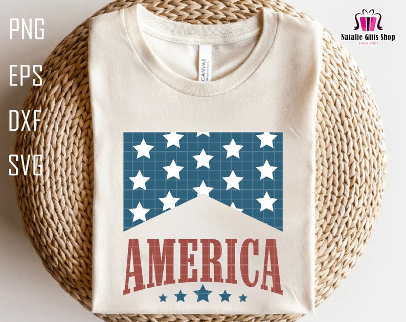 May include: A white t-shirt with a blue and white American flag design and the word "AMERICA" in red letters. There are five small stars below the word "AMERICA".
