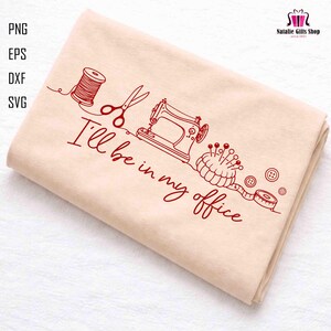 May include: A folded beige fabric with a red line drawing of sewing tools, including a spool of thread, scissors, a sewing machine, a pincushion, buttons, and a measuring tape. The text "I'll be in my office" is also included.
