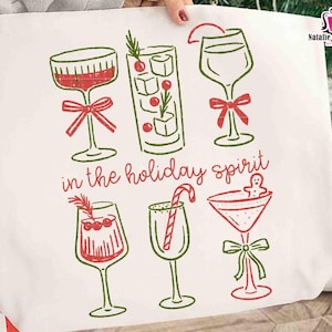 May include: Off-white tote bag featuring a festive design with six different cocktail glasses in red and green. The phrase "in the holiday spirit" is written in cursive. The bag has a simple, line-art style.