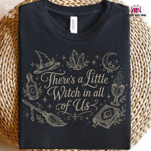 Può includere: Una t-shirt nera con una stampa grafica color oro che riporta il testo "There's a Little Witch in all of Us". Il design include illustrazioni di un cappello da strega, cristalli, una luna crescente, una boccetta, una scopa e un libro.