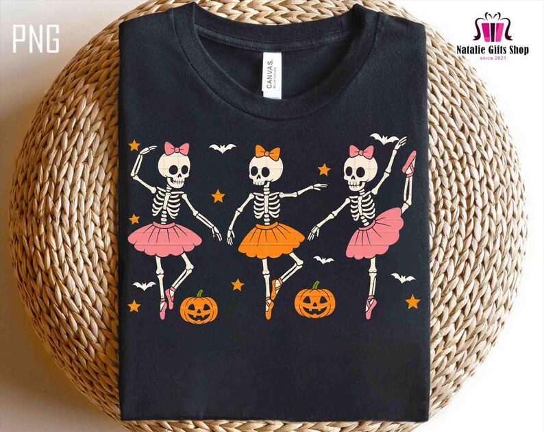 Puede incluir: Camiseta negra con un dise&ntilde;o de Halloween de tres bailarinas esqueleto con tut&uacute;s rosas y naranjas, lazos y zapatillas de ballet. El dise&ntilde;o incluye murci&eacute;lagos, estrellas y calabazas. La camiseta tiene una etiqueta "CANVAS".