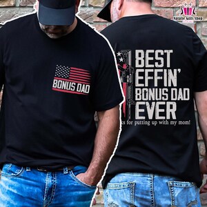 May include: Black t-shirts with the text "BONUS DAD" and "BEST EFFIN' BONUS DAD EVER" in white. The front of the shirt has an American flag design. The back of the shirt has a graphic of a rifle and the text "ks for putting up with my mom!"
