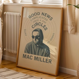 May include: A framed poster featuring Mac Miller with the text "Good News" and "Circles." The poster has a beige background with a portrait of Mac Miller wearing sunglasses and a hoodie. The frame is made of wood.