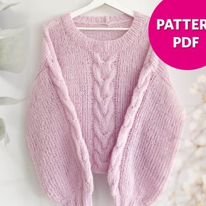 May include: A pink knitted sweater with a cable knit pattern. The sweater has long sleeves and a round neckline.