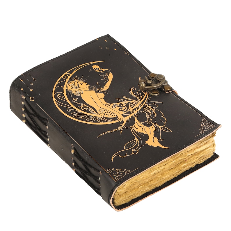 May include: Black leather journal with a gold mermaid design and a brass clasp. The journal has a distressed look and is perfect for writing or sketching.