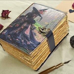 Puede incluir: Un diario de estilo vintage con una cubierta decorativa que presenta a una mujer con un vestido y sombrero negros. El diario tiene p&aacute;ginas envejecidas y amarillentas, una correa de cuero negro y un cierre de metal. Rosas secas y una bola decorativa est&aacute;n cerca.