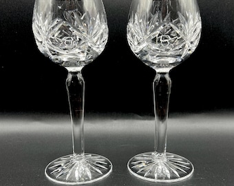 May include: Two clear crystal wine glasses with a cut glass design. The glasses have a tall stem and a round bowl.