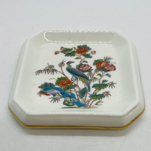 May include: A white porcelain dish with a gold rim features a colorful floral design with a blue bird perched on a branch. The design includes pink, orange, and green flowers.