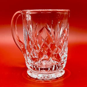 Puede incluir: Una taza de cerámica blanca con un asa negra y el texto "But First, Coffee" en negrita negra. La taza se muestra sobre una superficie blanca. La taza mide aproximadamente 10 cm de alto.