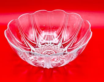 May include: A clear glass bowl with a scalloped rim and a detailed, geometric pattern at the base. The bowl has a flower-like shape and is set against a vibrant red background, highlighting its elegant design.