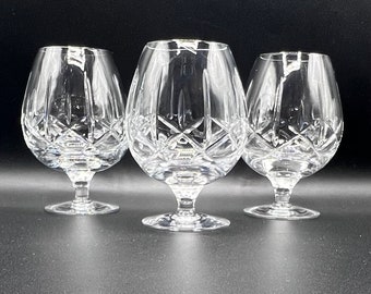 May include: Three clear glass brandy snifters with a cut crystal design. The glasses are on a black surface.