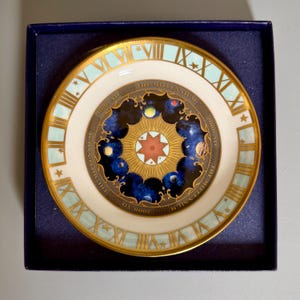 May include: A decorative plate with a cream-colored background, gold trim, and Roman numerals. The center features a celestial design with planets and stars, and the text "THE MILLENNIUM 2000 AD". The plate is in a blue box.