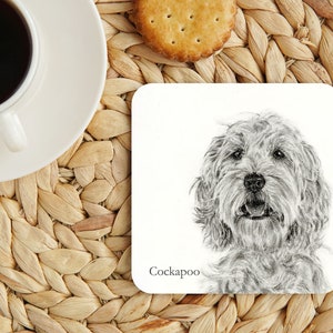 May include: A white ceramic coaster with a black and white pencil drawing of a Cockapoo dog. The coaster has the word "Cockapoo" printed in black text at the bottom.