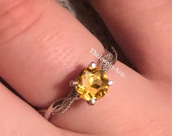 May include: A silver ring with a twisted band and a round, yellow citrine gemstone.