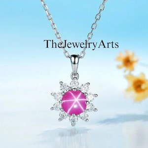 May include: A silver necklace with a pink star sapphire pendant surrounded by a halo of smaller diamonds. The pendant is in the shape of a sunburst.