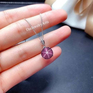 May include: A silver necklace with a round pendant featuring a star ruby gemstone. The pendant has a starburst pattern and is set in a silver bezel.