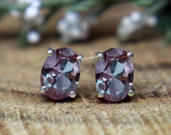Peut inclure: Une paire de boucles d'oreilles à clous en pierres précieuses de forme ovale. Les pierres précieuses sont un mélange de teintes violettes et roses, serties dans un métal argenté. Les boucles d'oreilles sont présentées sur une surface en bois.