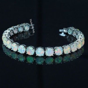 May include: A silver tennis bracelet featuring a row of white opal stones. The bracelet is displayed against a black background and reflects light.