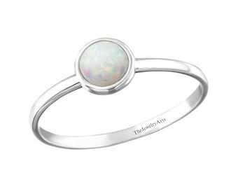 Pode incluir: Um anel de prata com uma pedra de opala branca. O anel é gravado com "TheJewelryArts".