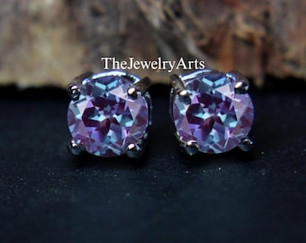 Peut inclure: Une paire de boucles d'oreilles à clous rondes avec des pierres précieuses alexandrite changeant de couleur. Les pierres présentent un mélange de teintes violettes et sarcelle, serties dans un métal argenté. Les boucles d'oreilles sont de TheJewelryArts.