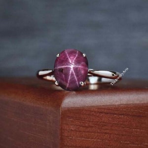 May include: A silver ring featuring a large, oval-shaped, red ruby gemstone. The ruby has a star-shaped pattern inside.