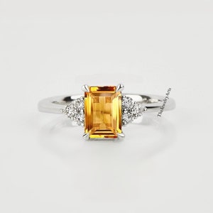 May include: A silver ring featuring a large, rectangular, yellow citrine gemstone with smaller, round, white diamonds on either side. The ring is set in a simple, elegant style.