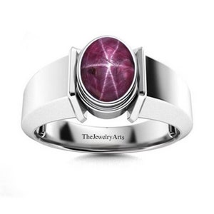 May include: A silver ring with a pink star ruby gemstone. The ring has a simple band and a bezel setting for the stone. The text "TheJewelryArts" is engraved on the inside of the band.