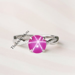 Op de afbeelding: Een zilveren ring met een roze ster-saffier edelsteen en een gedraaide band versierd met kleine diamanten.