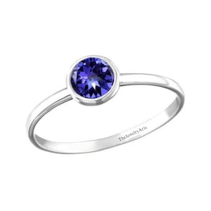 May include: A silver ring with a bezel setting featuring a round, dark blue gemstone. The ring is inscribed with the text "TheJewelryArts".