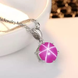 May include: A silver chain necklace with a pendant featuring a pink star ruby gemstone.