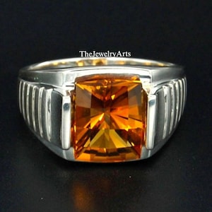 Puede incluir: Un anillo de plata con una gran piedra preciosa naranja de corte cuadrado. El anillo tiene una banda texturizada con líneas verticales.