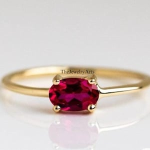 Peut inclure: Une délicate bague en or avec une seule pierre précieuse de rubis de forme ovale. Le rubis est de couleur rouge foncé et est serti dans un design simple et élégant.