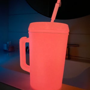 Op de afbeelding: Een witte plastic beker met een handvat en een rietje, die roze gloeit in het donker.
