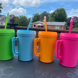 Op de afbeelding: Vier plastic bekers met handvatten en rietjes. De bekers zijn groen, blauw, oranje en roze.